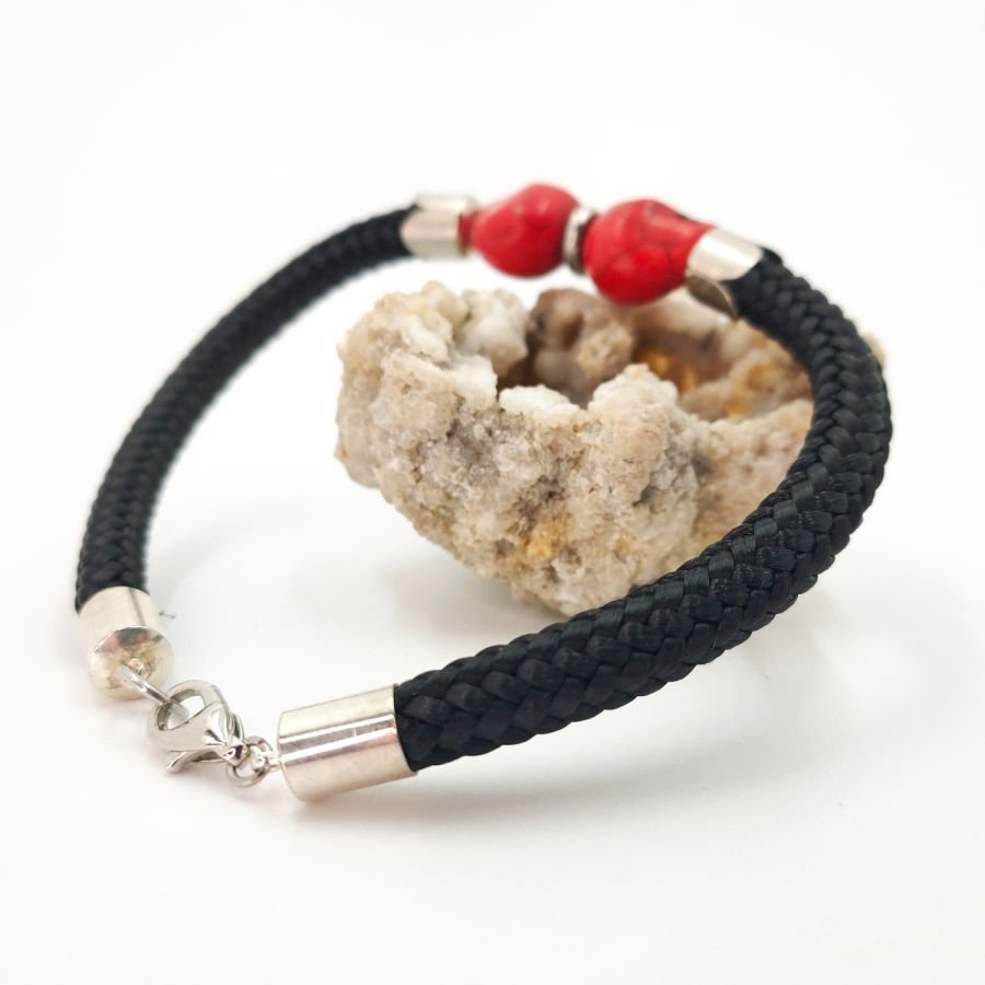 Pulsera doble de calavera y tibias cruzadas con piedras rojas sobre una gruesa cuerda negra