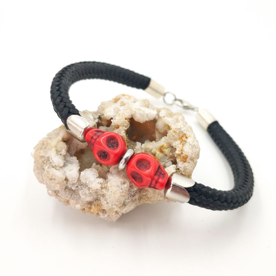 Pulsera doble de calavera y tibias cruzadas con piedras rojas sobre una gruesa cuerda negra